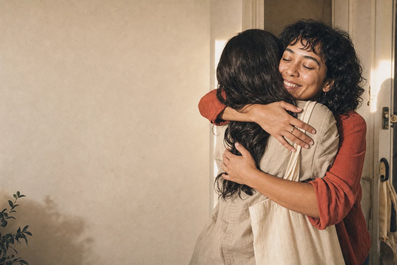Two longtime friends hugging in an apartment doorway.